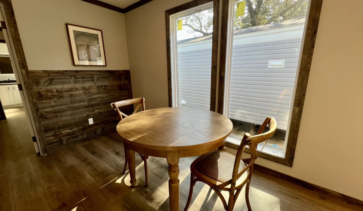 Round wooden dining table with two chairs in a well-lit interior, showcasing manufactured home features and modern design elements.