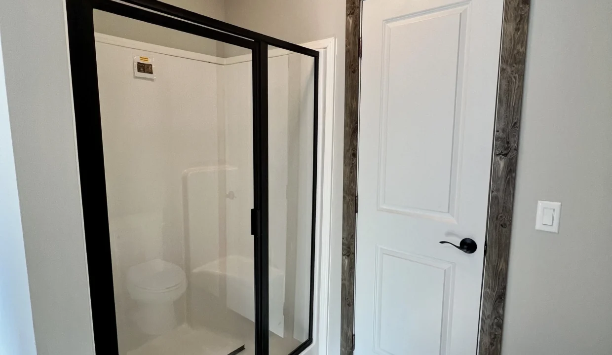Modern bathroom interior featuring a glass shower enclosure and white door, showcasing the Bandit manufactured home's design and amenities.