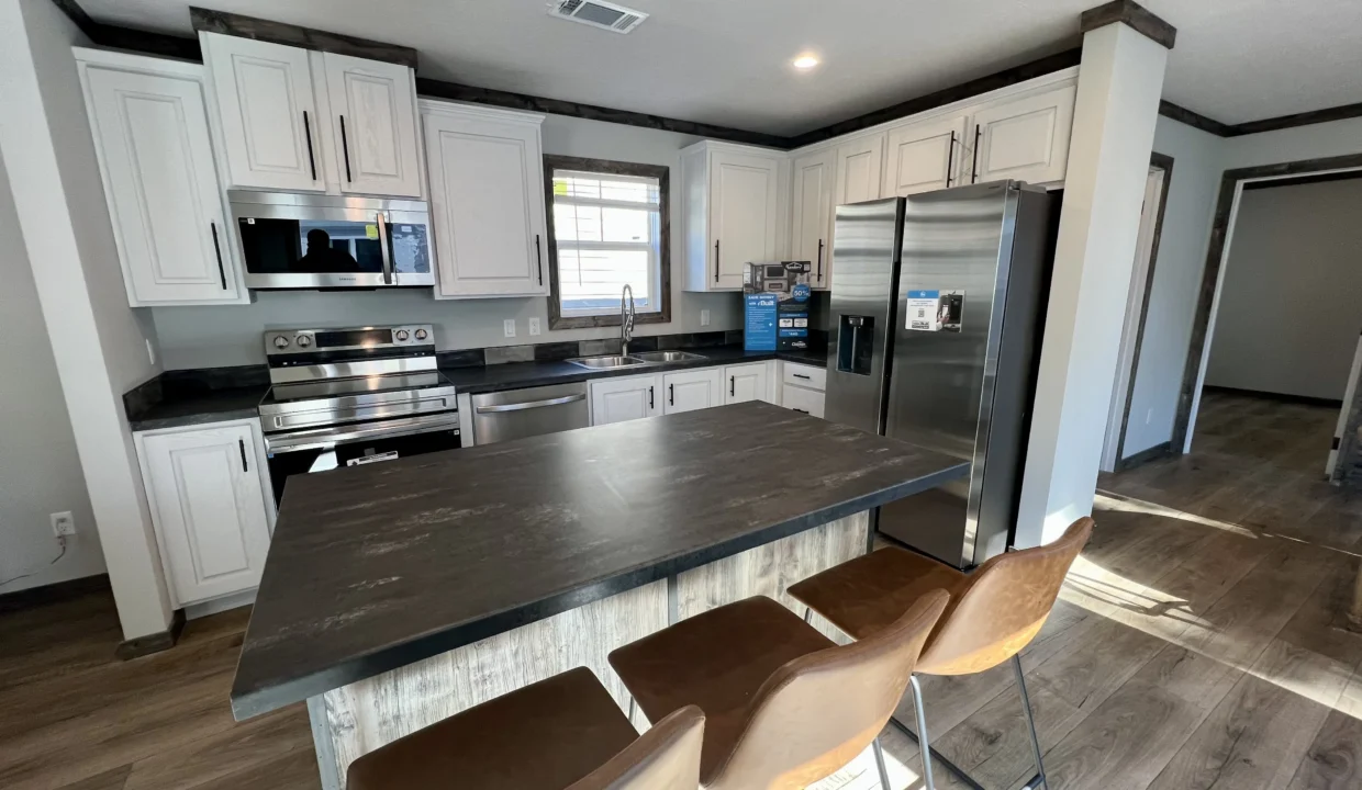 Modern kitchen interior featuring stainless steel appliances, white cabinetry, and a dark countertop, highlighting the Bandit manufactured home's design and layout.