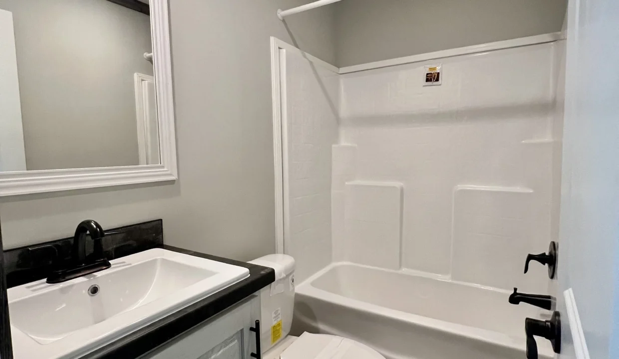 Bathroom interior featuring a modern sink with black faucet, a white bathtub with shower, and a large mirror, highlighting the Bandit manufactured home's bathroom design.