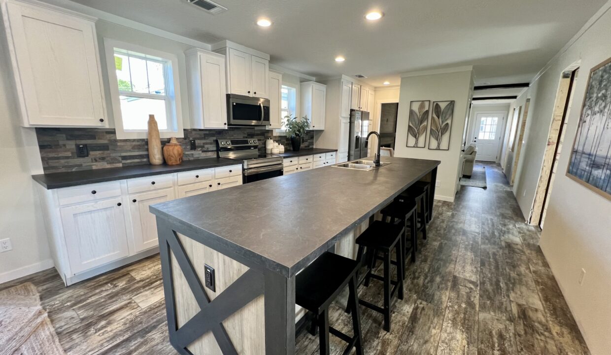 Modern kitchen interior of Boujee XL manufactured home featuring spacious island, stainless steel appliances, white cabinetry, and decorative elements.