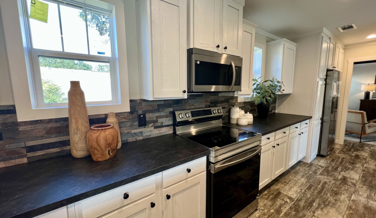 Modern kitchen featuring stainless steel appliances, dark countertops, decorative vases, and a stylish backsplash, showcasing the Boujee XL manufactured home by Sanders Housing.