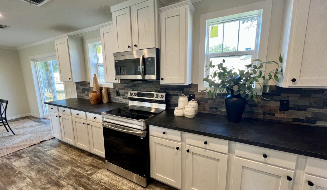 Modern kitchen interior featuring stainless steel appliances, white cabinetry, and a stone backsplash, highlighting the Boujee XL manufactured home's gourmet kitchen design.