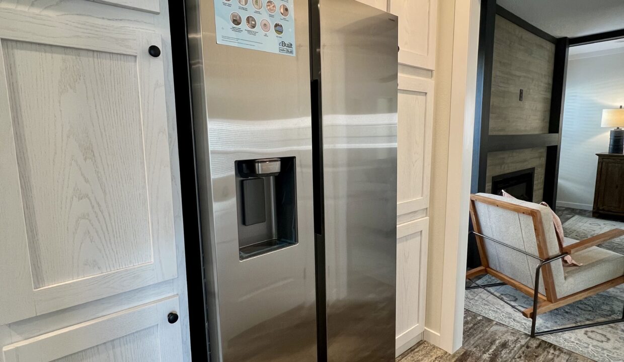Stainless steel refrigerator with water dispenser and cabinetry in a modern manufactured home interior, highlighting the Boujee XL model's gourmet kitchen features.