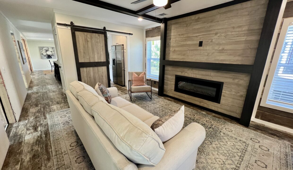 Spacious living room in Boujee XL manufactured home featuring modern decor, plush sofa, accent chair, and stylish fireplace.