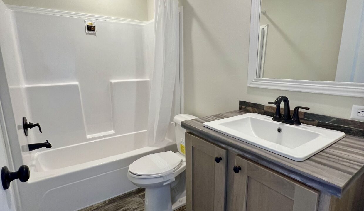 Modern bathroom featuring a bathtub with shower, white vanity sink with black faucet, and neutral-colored walls, highlighting the Boujee XL manufactured home by Sanders Housing.