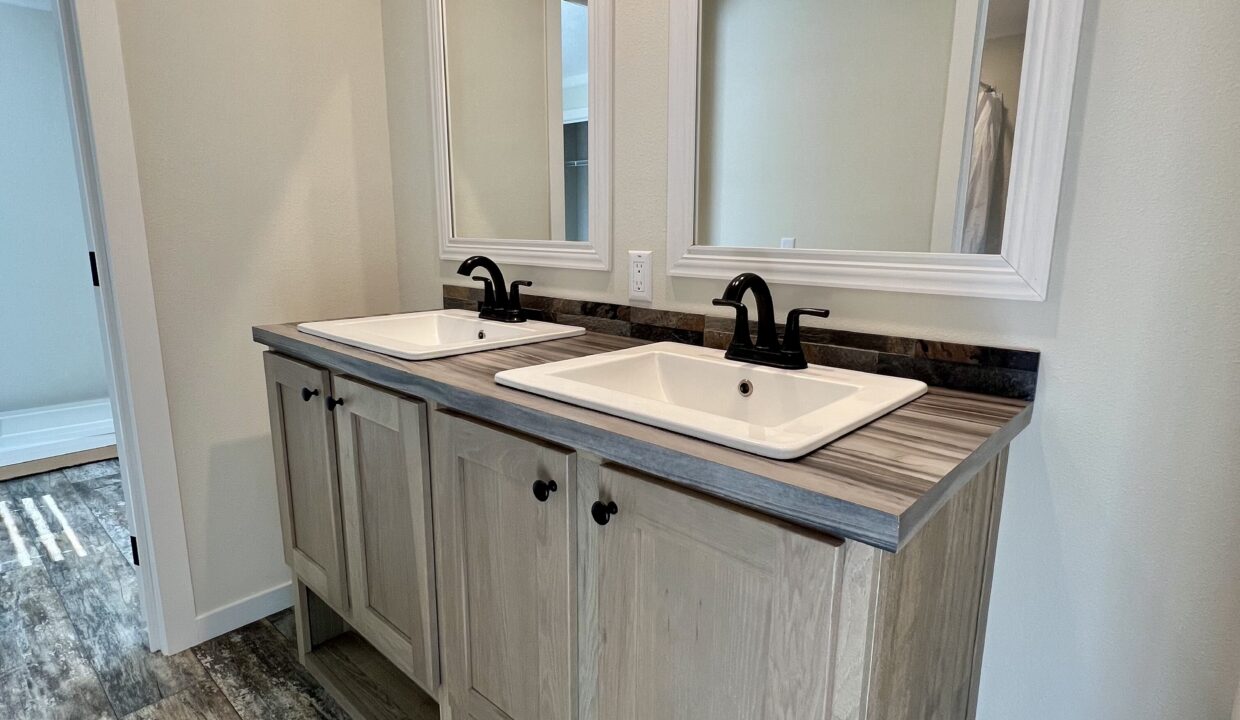 Double sink vanity with modern black faucets and wooden cabinetry in a spacious bathroom setting, showcasing the luxurious features of the Boujee XL manufactured home by Sanders Housing.