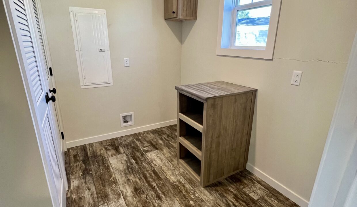 Interior view of the Boujee XL manufactured home showcasing a small room with a wooden cabinet and window, highlighting modern design elements and spacious layout.
