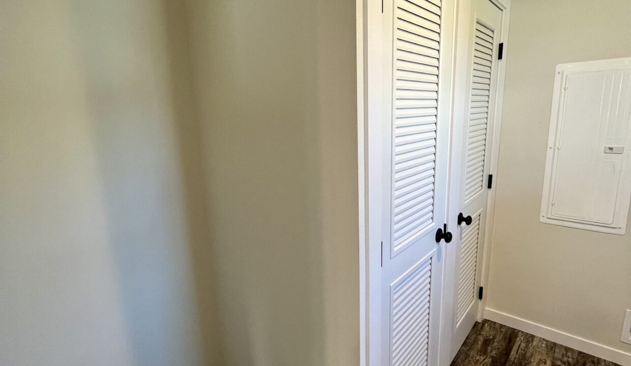 Interior view of a Boujee XL manufactured home featuring white louvered closet doors and a wall-mounted electrical panel, showcasing spacious and modern design elements.