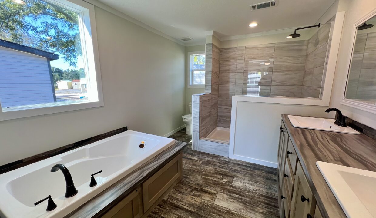 Modern bathroom interior featuring a spacious soaking tub, dual sinks with black faucets, and a separate shower area, showcasing the luxurious design of the Boujee XL manufactured home by Sanders Housing.