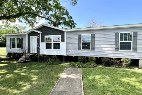Elegant manufactured home with modern design, featuring a front entry, multiple windows, and landscaped yard, available for sale through Sanders Housing in Pensacola, FL.