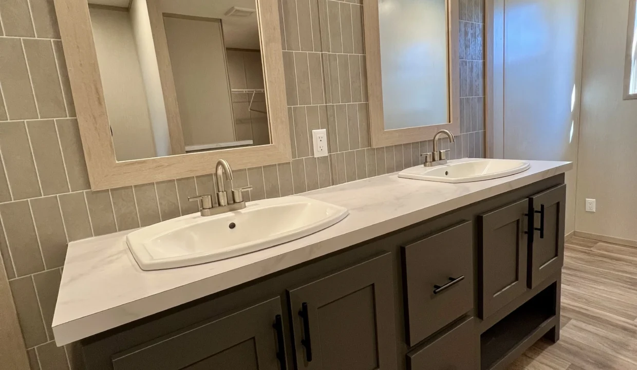 Modern bathroom with double sinks, stylish faucets, gray tiled walls, and ample storage in a manufactured home setting.