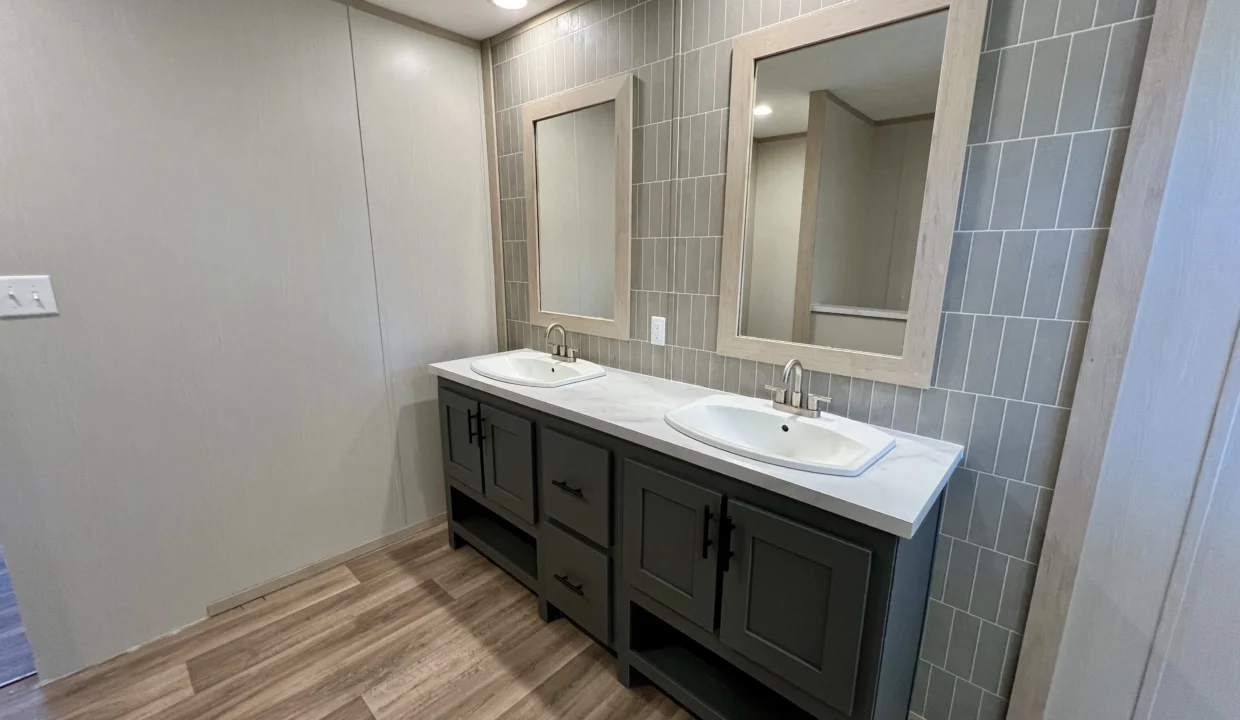 Modern bathroom featuring dual sinks, gray cabinetry, and stylish tile accents, showcasing the Snowcap manufactured home's interior design.